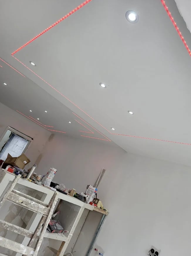 Interior ceiling under construction with drywall, recessed lights, and red electrical wiring visible against gray ceiling.
