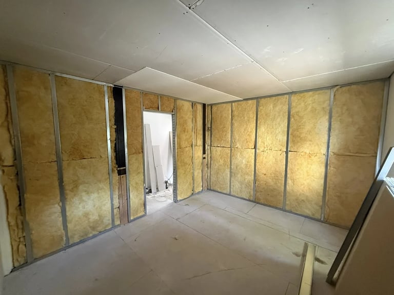 Interior construction room with yellow insulation panels on walls, concrete subfloor, and open doorway to hallway